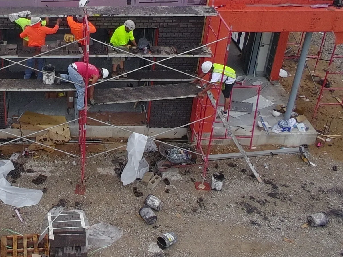 Masons on scaffolding laying dark brick veneer on a new commercial building, seen from above, brick masonry