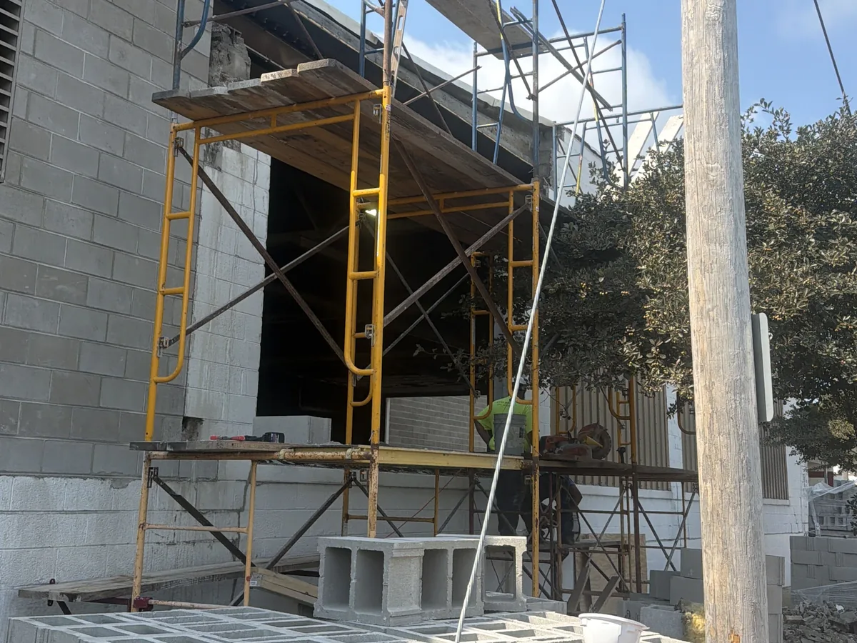 Concrete block walls with steel scaffolding, stacked block in front and a masonry saw on the plank, block walls