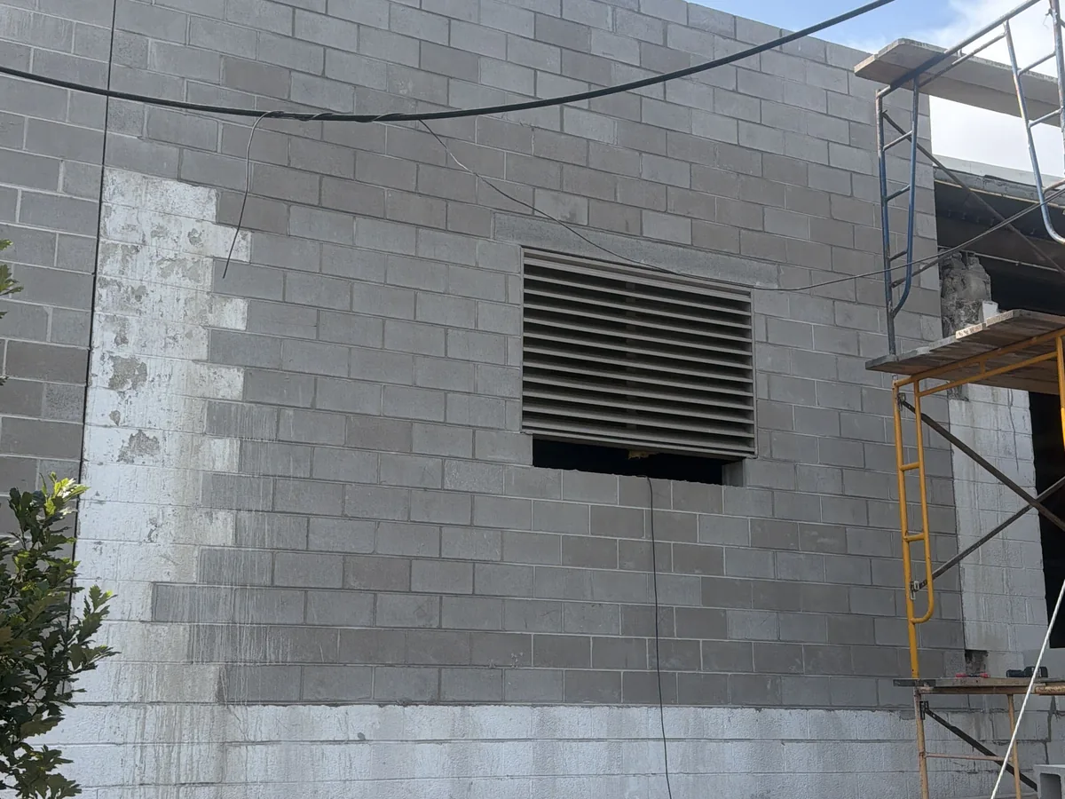 Concrete block wall with a louvered vent opening and steel scaffolding set against it, block foundations and block walls