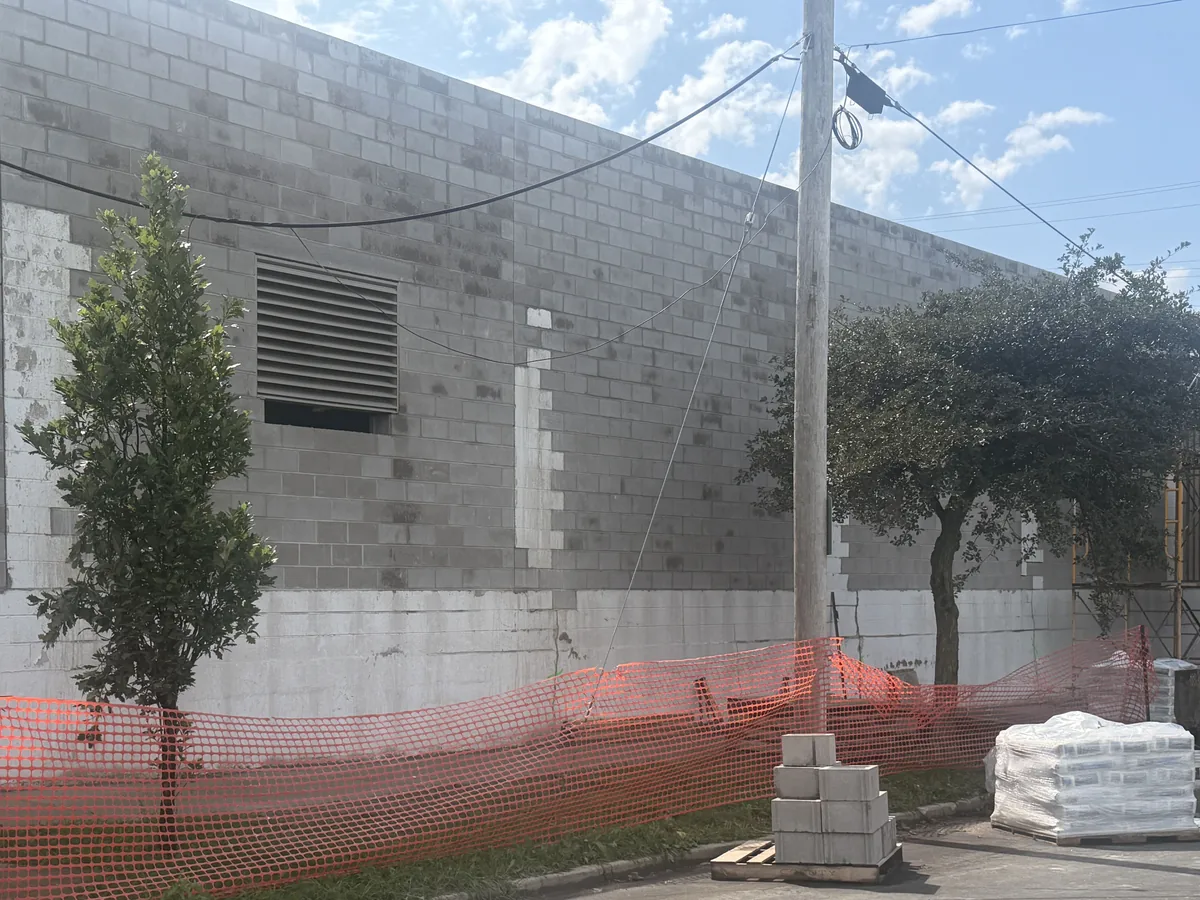 Long concrete block wall with orange safety fence and pallets of block along the base, block walls
