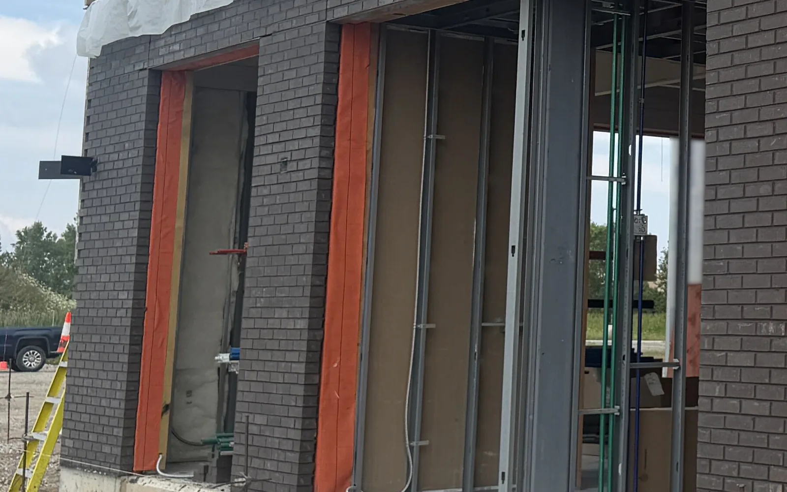 Dark brick veneer piers framing wrapped storefront openings on a commercial building under construction, brick masonry