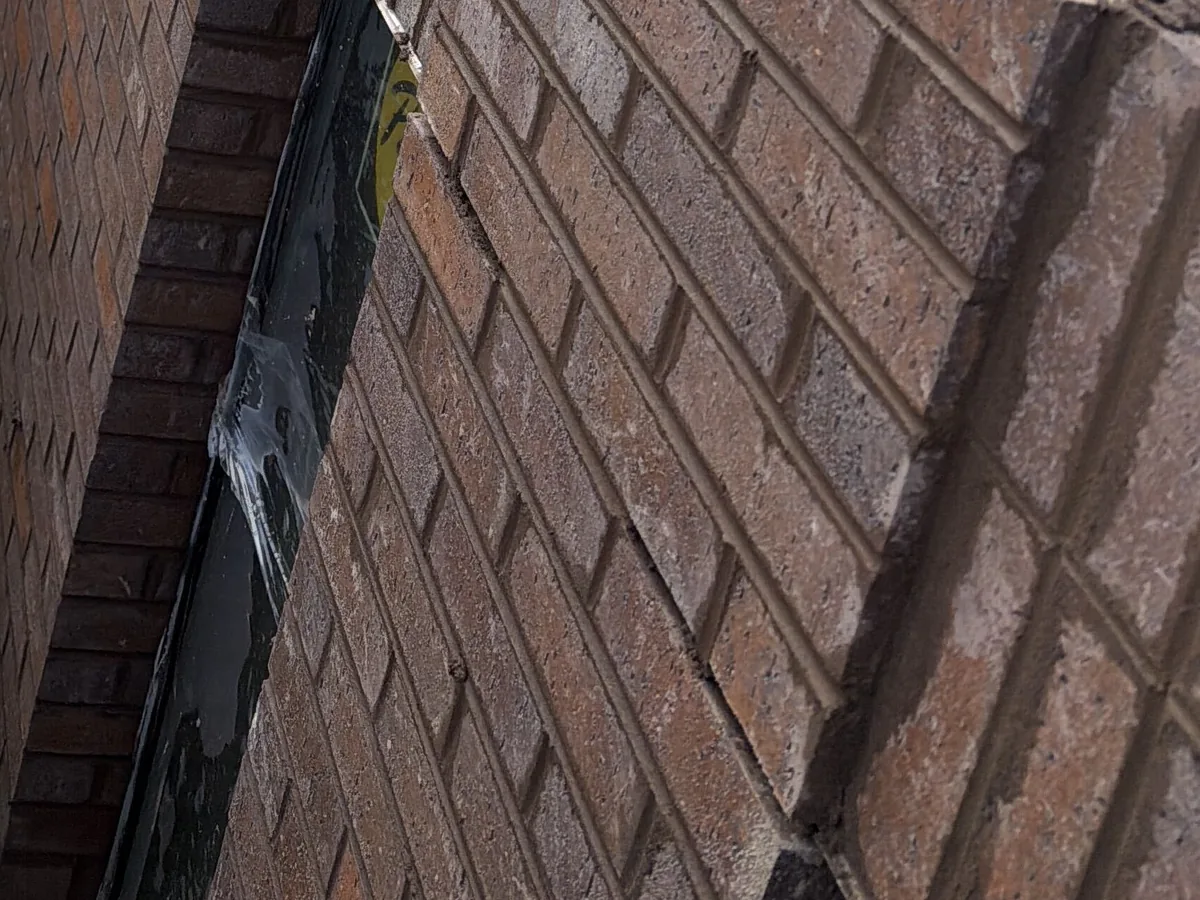 Close view of new brick veneer courses with tooled mortar joints beside a flashed window opening, brick masonry