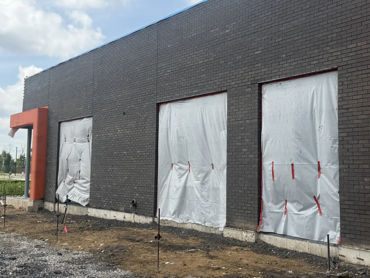 Long dark brick veneer wall with three openings covered in weather wrap on a new building, brick masonry