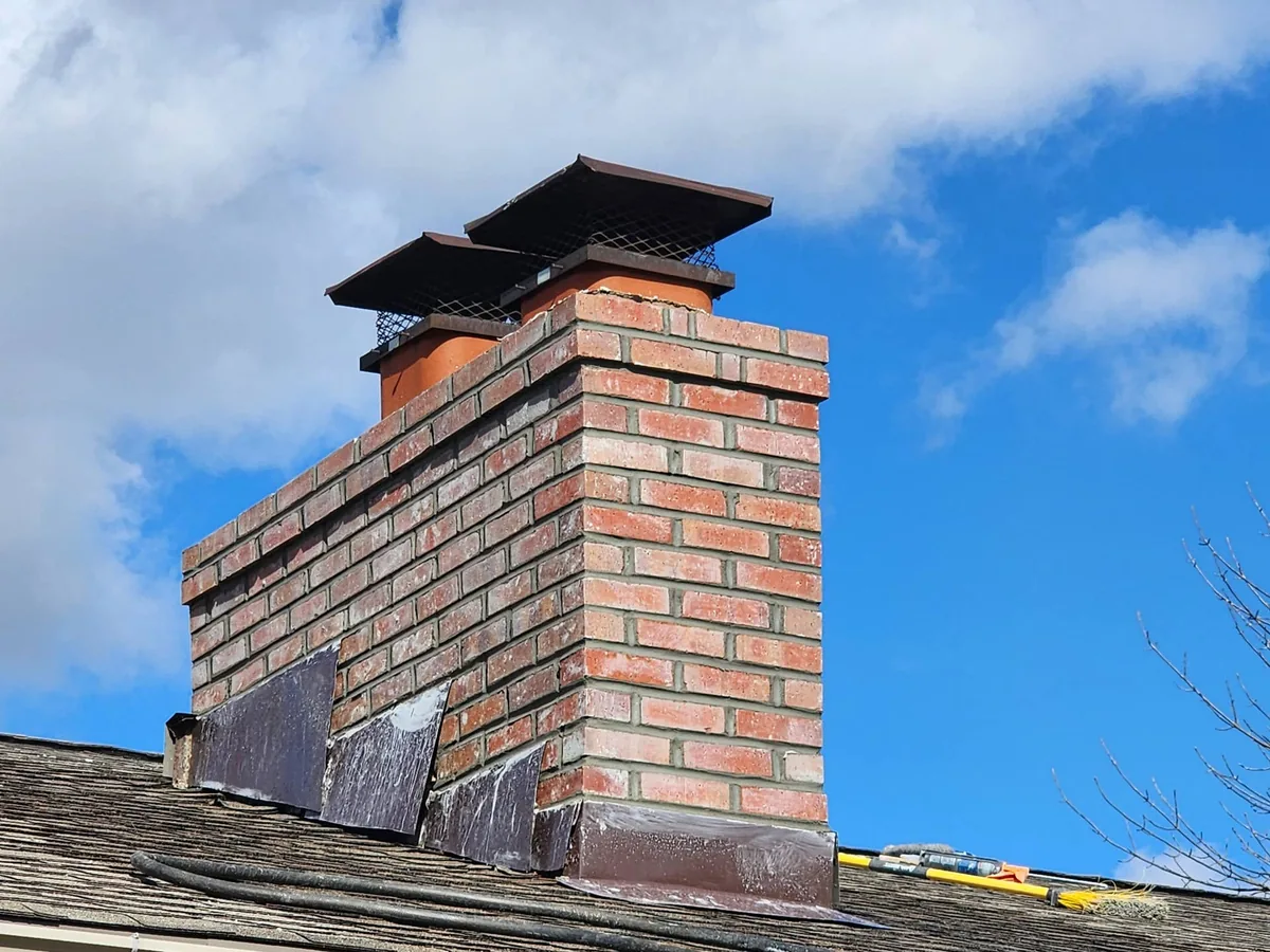 Rebuilt brick chimney top with new courses and two flue caps against a blue sky, chimney repair