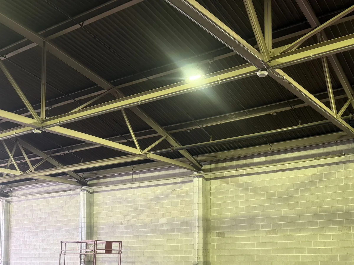 Interior of a building with tall concrete block walls under steel roof trusses and work lights, commercial masonry