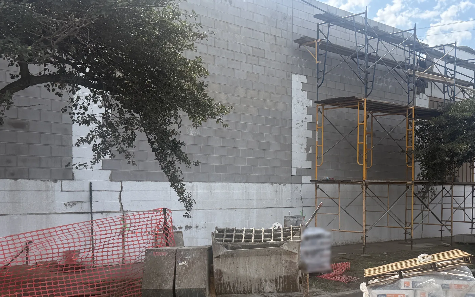 Concrete block wall on a commercial building with steel scaffolding, a mortar mixer and block stacked at the base, commercial masonry