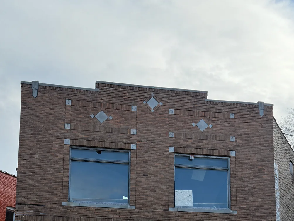Upper story of a two-story historic brick storefront with a diamond-pattern brick cornice, commercial masonry