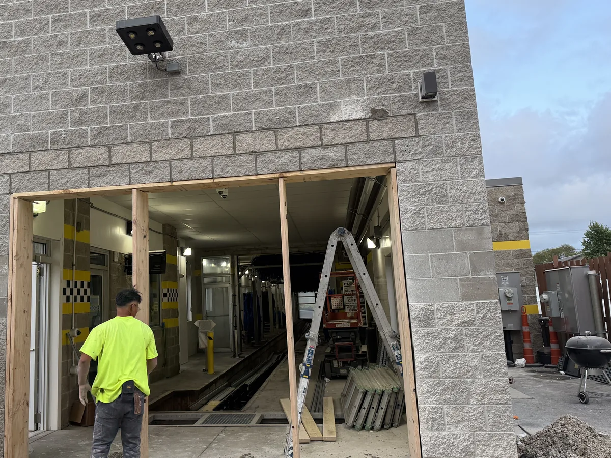 Split-face concrete block wall on a commercial building with a framed new opening and a worker seen from behind, commercial masonry