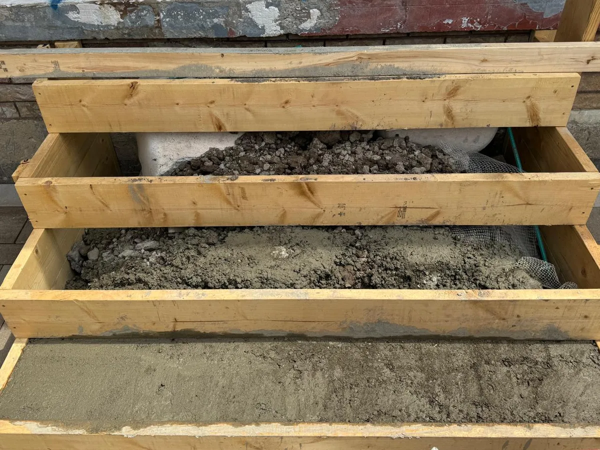 Wood forms for new concrete steps at a house entry with gravel fill and the bottom step poured, concrete work