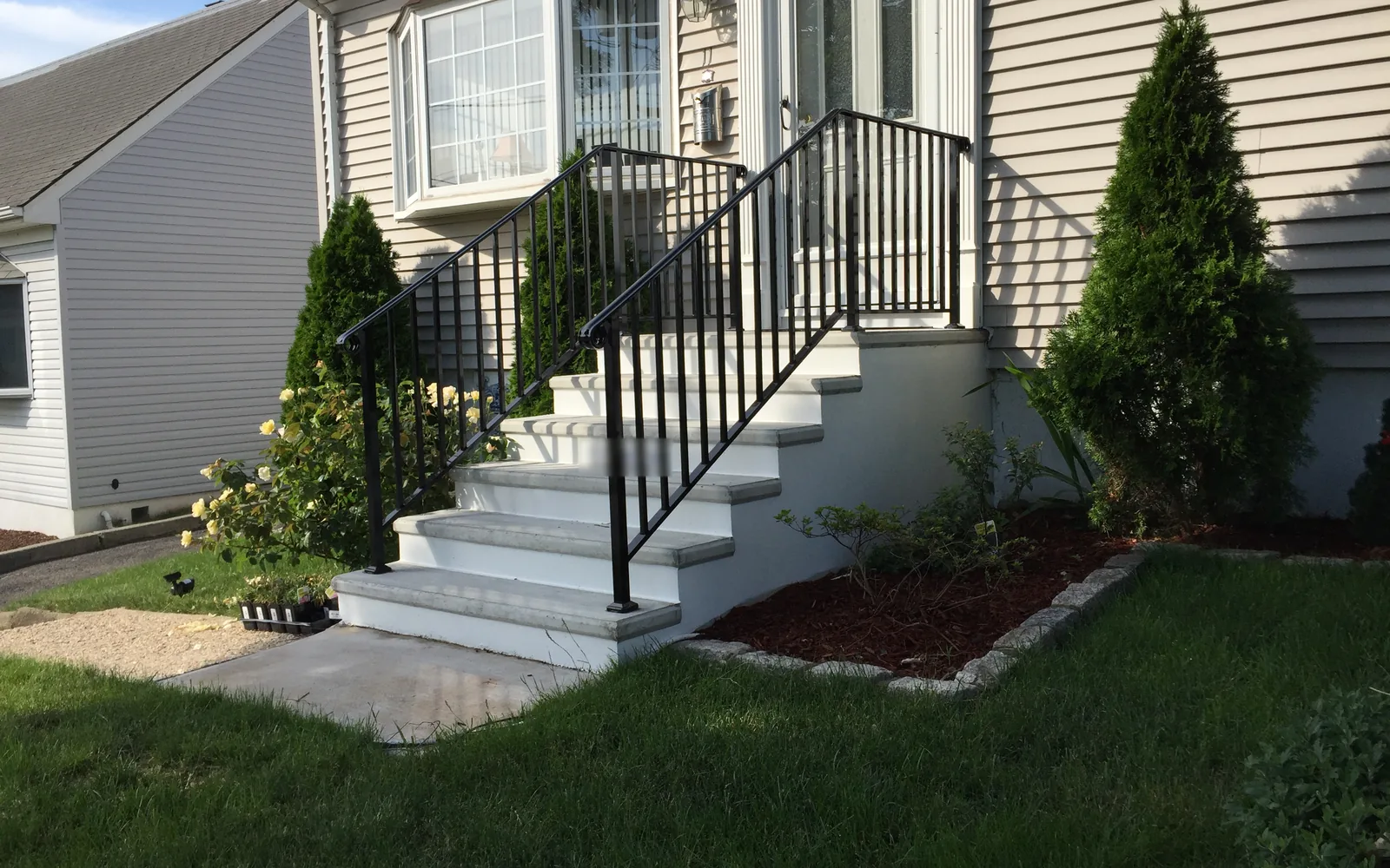 White concrete front steps with black metal railings leading to a house entry, concrete work