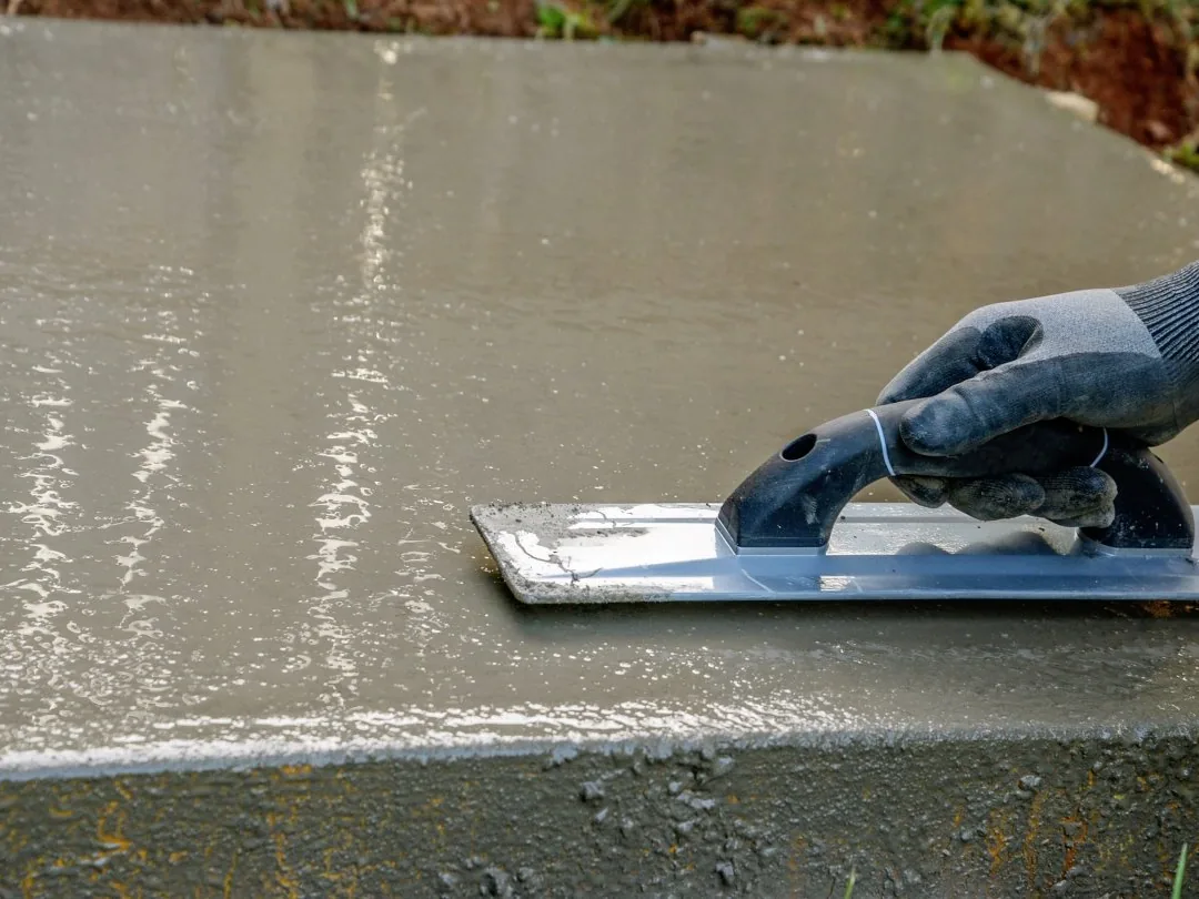 Gloved hand floating the wet surface of a freshly poured concrete slab, concrete work