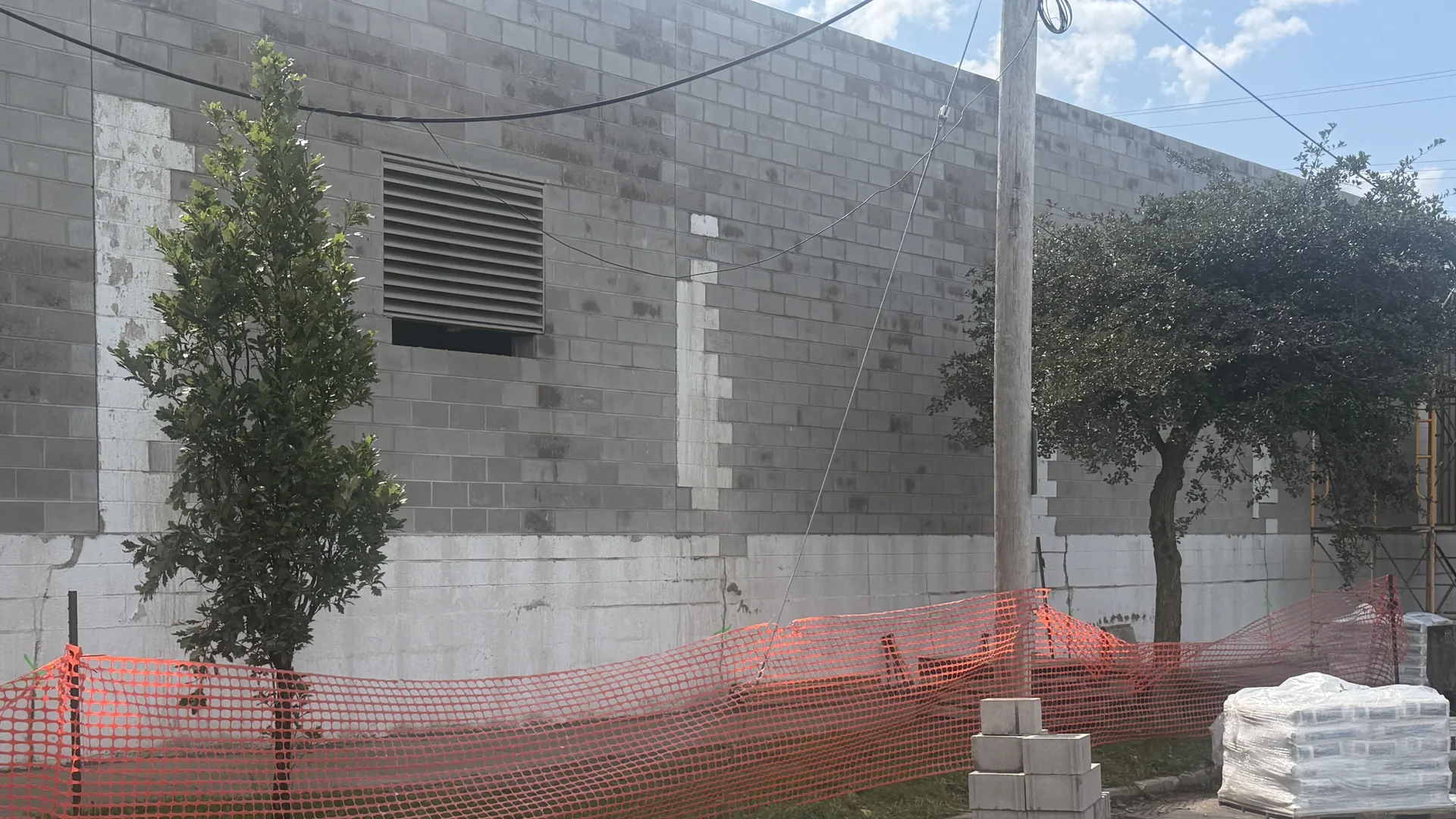 Concrete block wall with a louvered vent, a utility pole and orange safety fence along the base, block walls