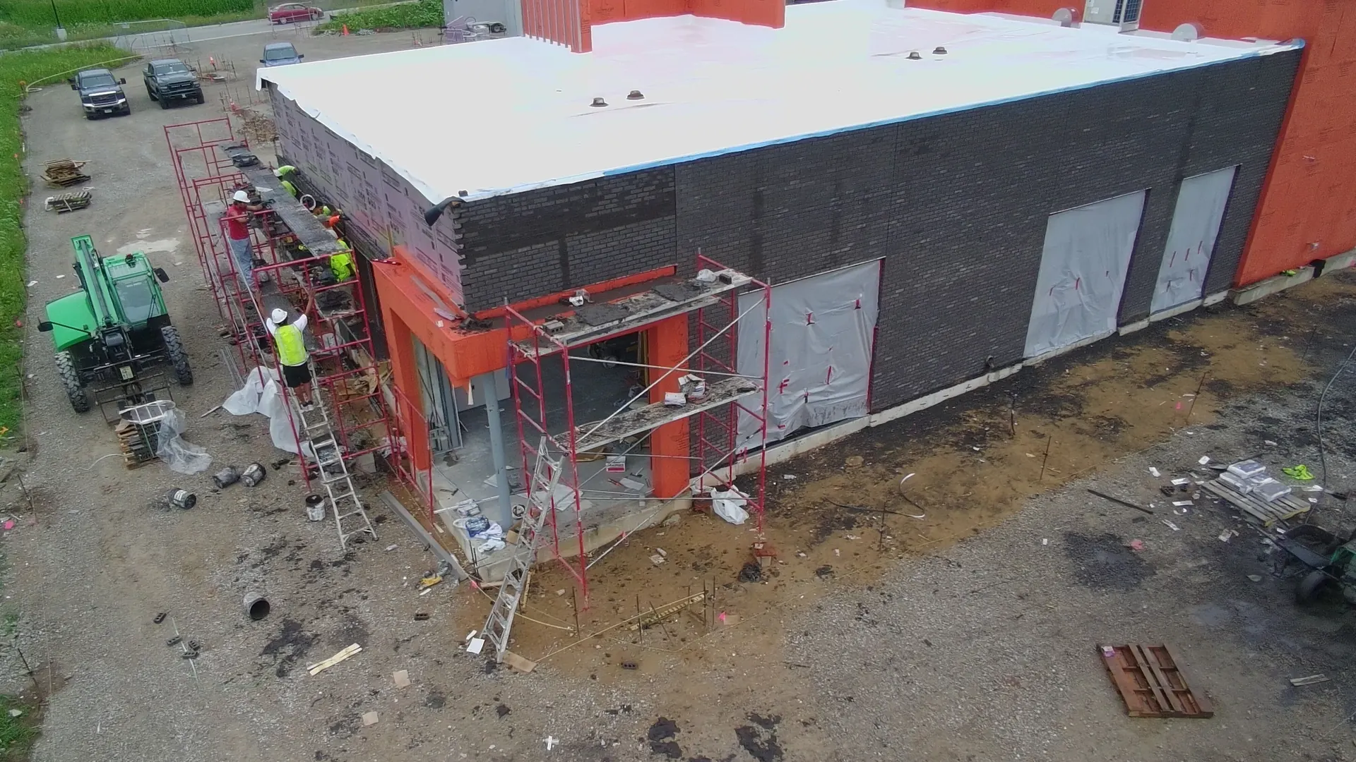 Aerial view of a new one-story commercial building with dark brick veneer going up over the block walls and masons on scaffolding, brick masonry