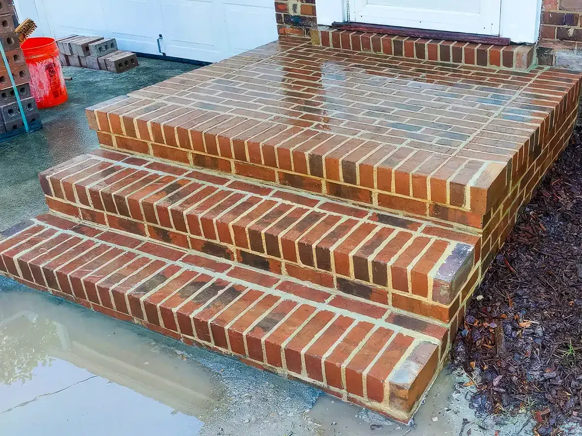 New brick steps and landing at a house entry with brick and tools stacked beside them, masonry repair