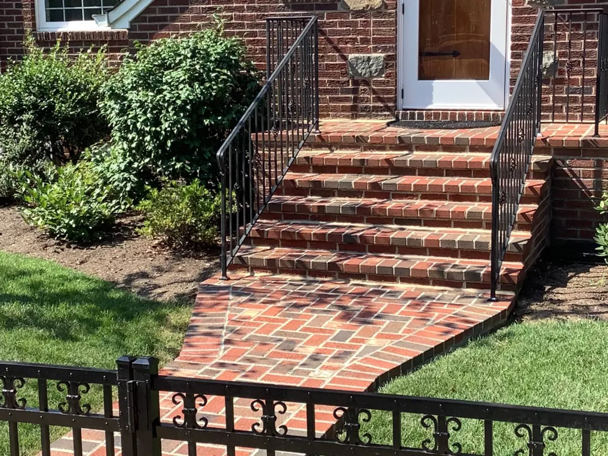 Red brick front steps, landing and walk with black iron railings at a brick house, masonry repair