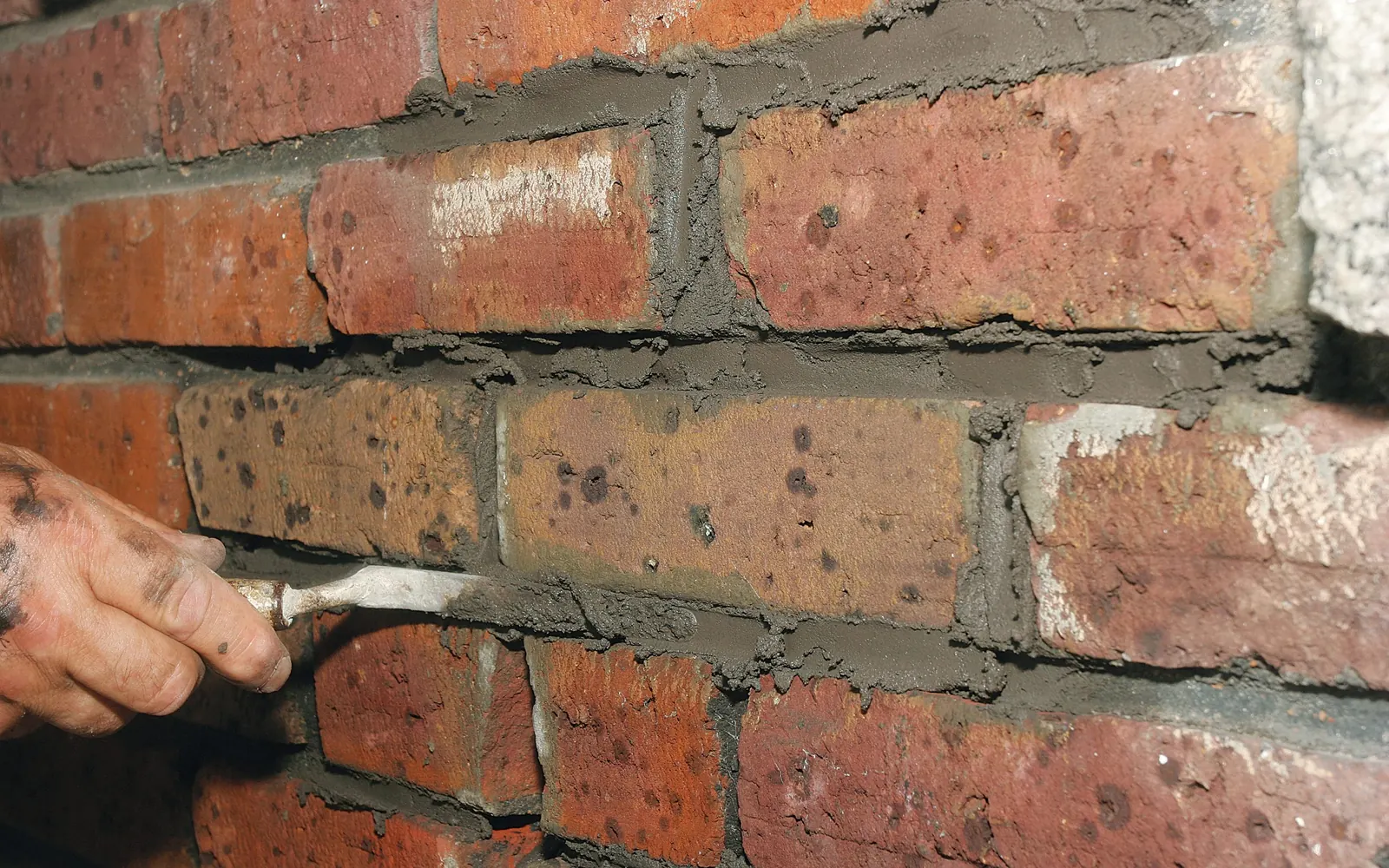 Hand pointing new mortar into the joints around a brick in an old red brick wall, masonry repair