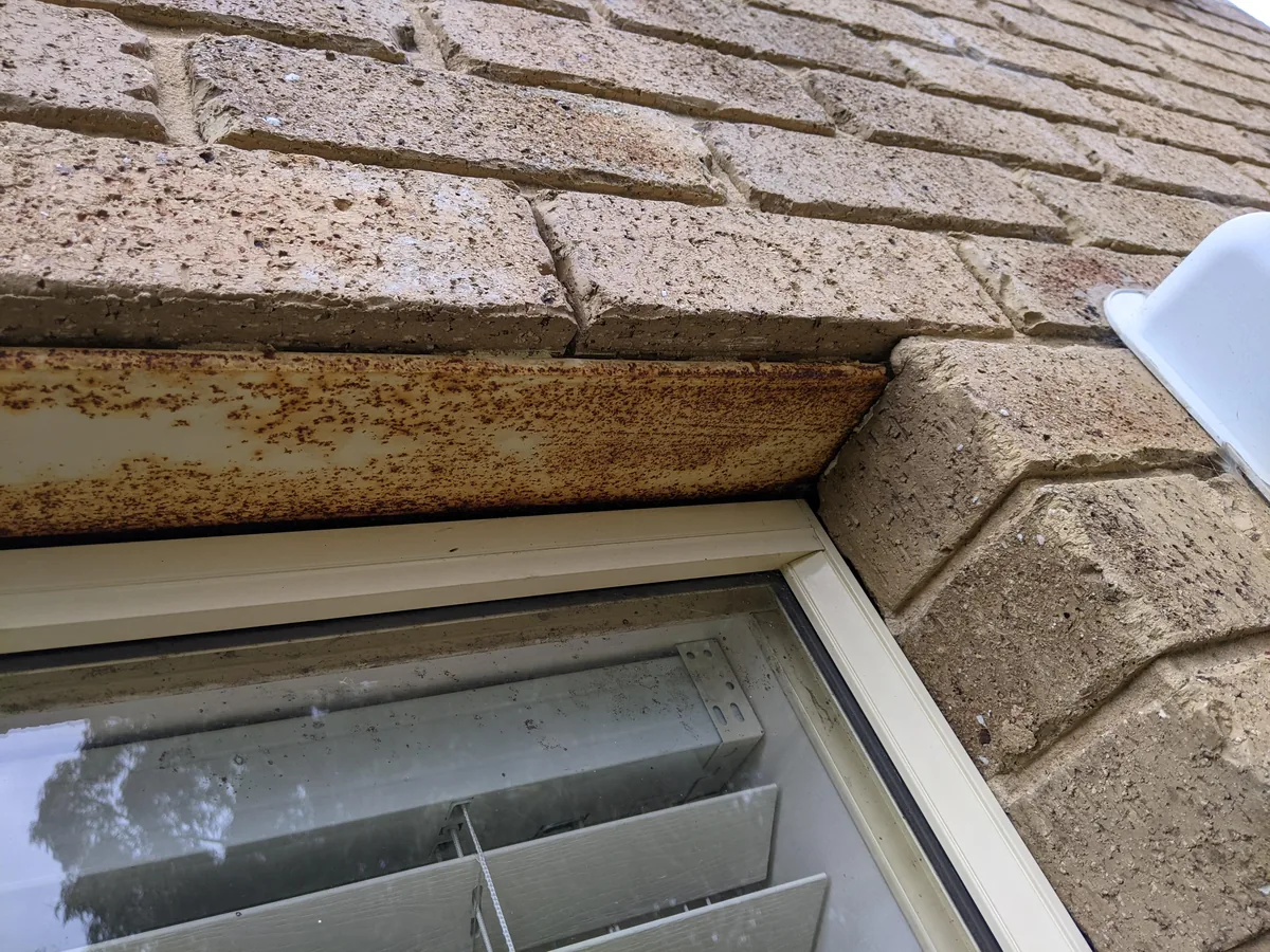 Rusted steel lintel over a window in a tan brick wall, masonry repair
