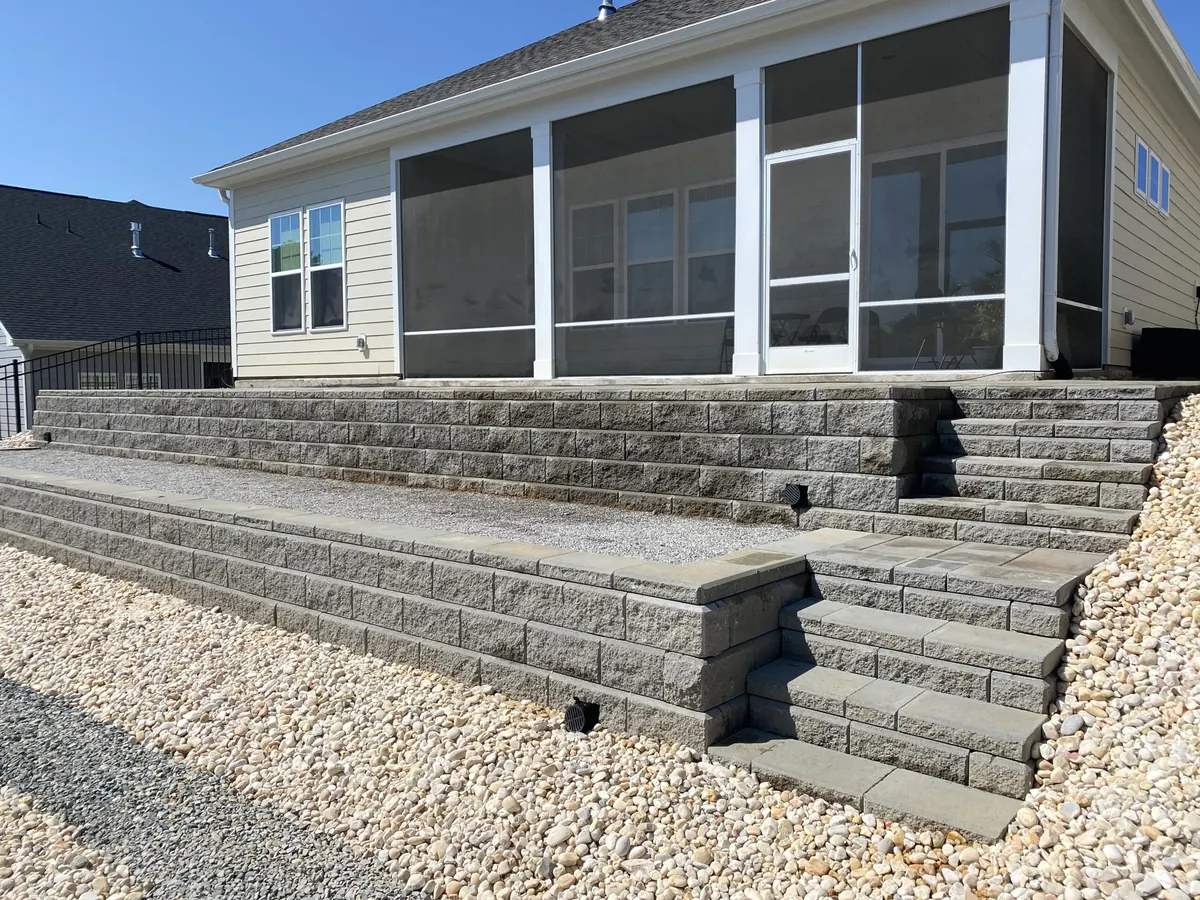 Long segmental block retaining wall with steps behind a house and river rock at the base, retaining walls