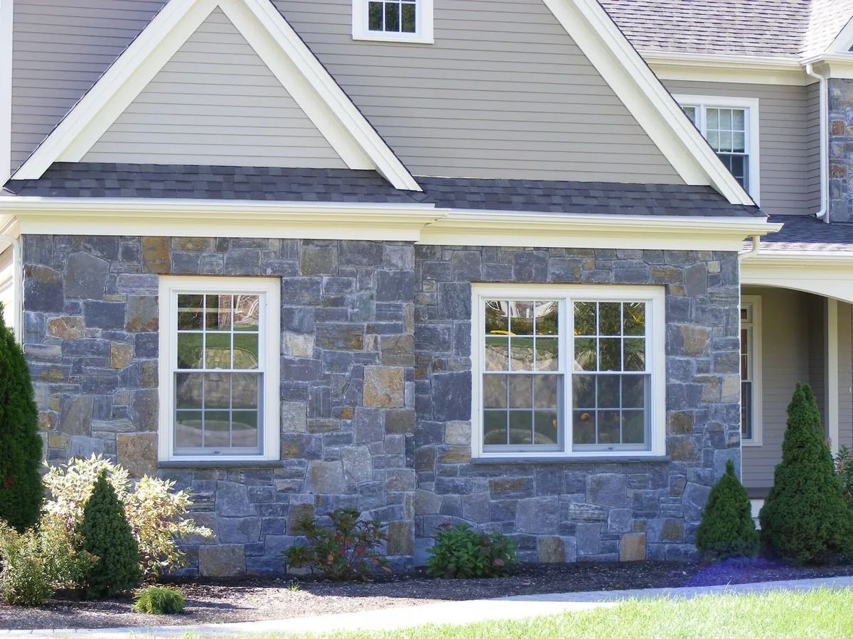 House front with gray natural stone veneer around white windows below lap siding, stone masonry