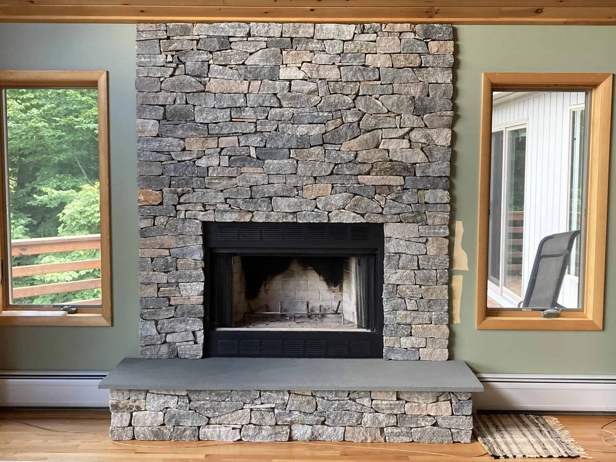 Stacked natural stone fireplace wall with a raised stone hearth between two windows, stone masonry