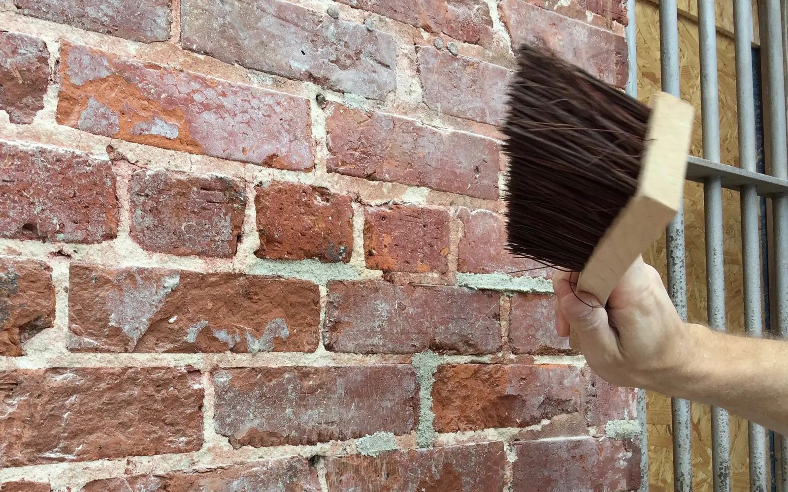 Hand brushing freshly repointed mortar joints on an old red brick wall, tuckpointing