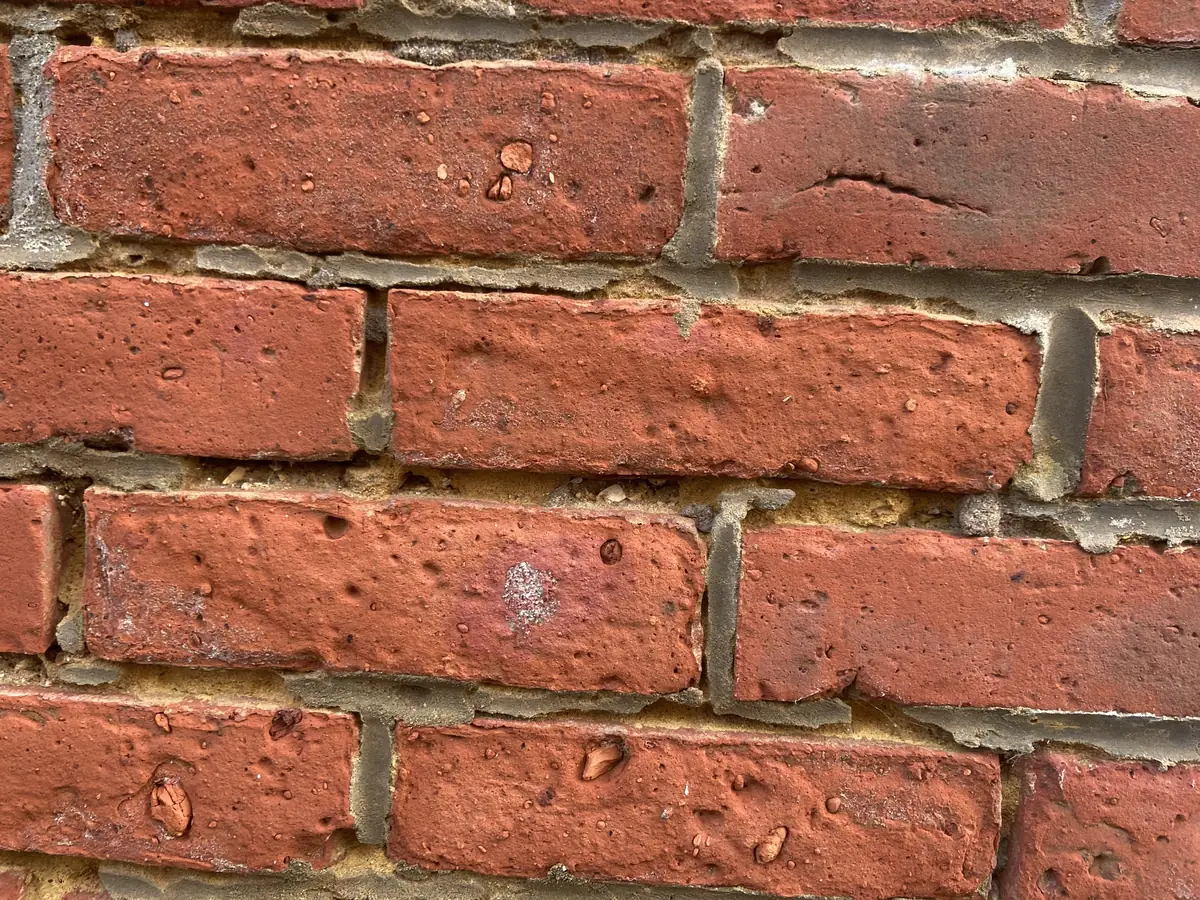 Close view of red brick with crumbling, recessed mortar joints that need repointing, tuckpointing