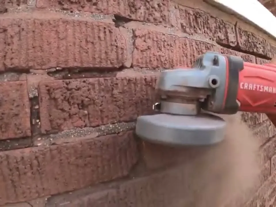 Angle grinder cutting out old mortar from the joints of a brick wall before repointing, tuckpointing