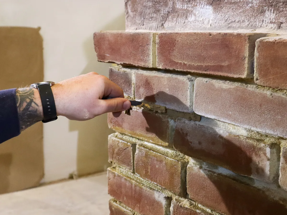 Hand pressing new mortar into brick joints with a tuck pointer, tuckpointing
